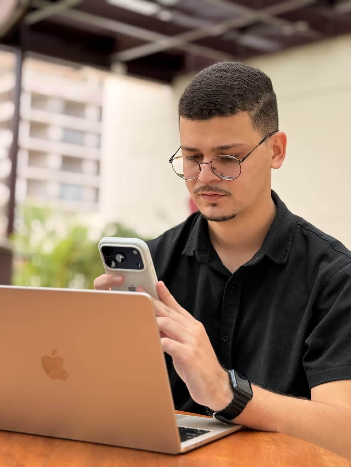 Abdeel de óculos olhando para o celular, com um notebook à frente