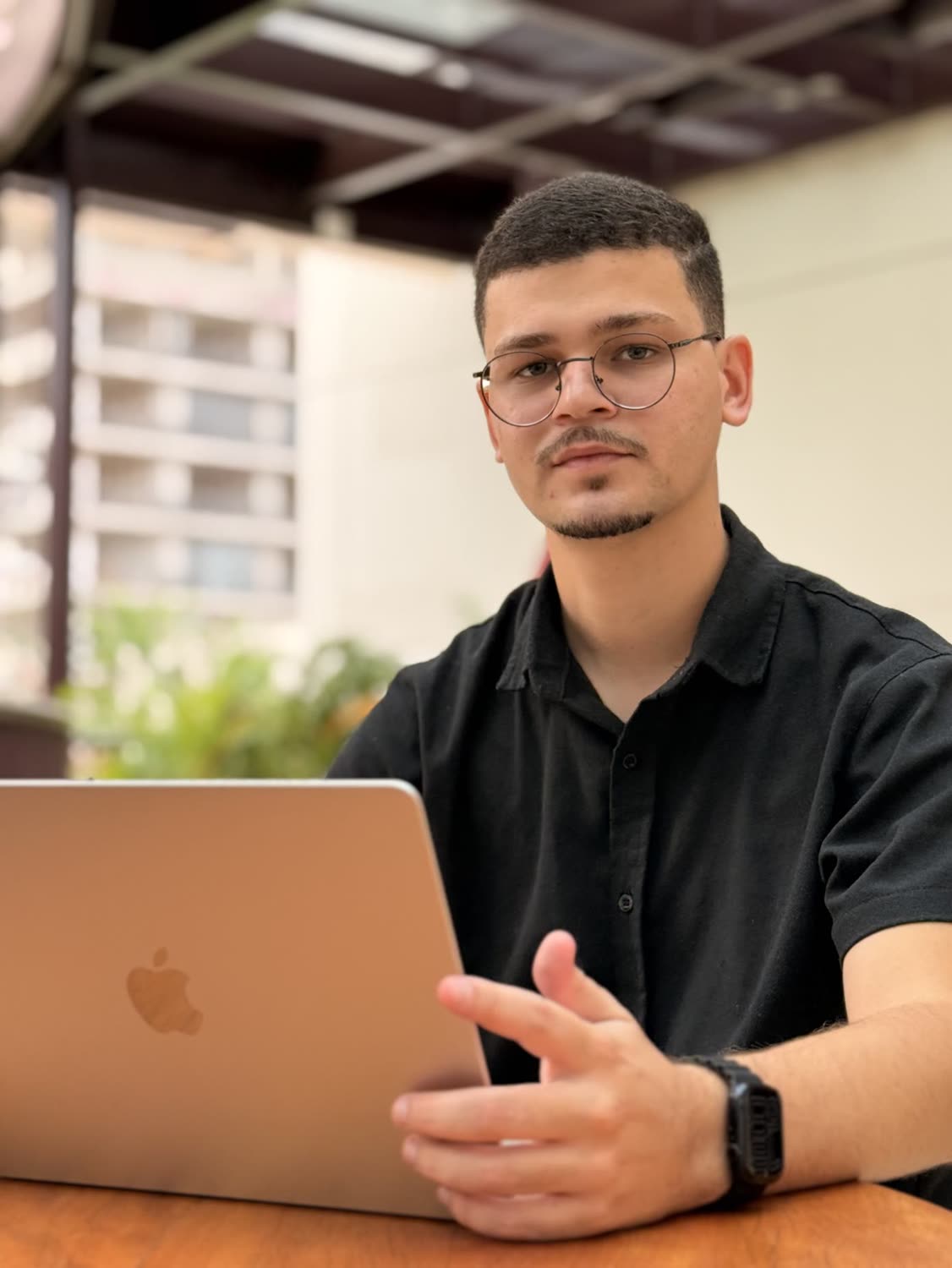 Abdeel de óculos e camisa preta, sentado diante de um notebook, explicando com a mão aberta