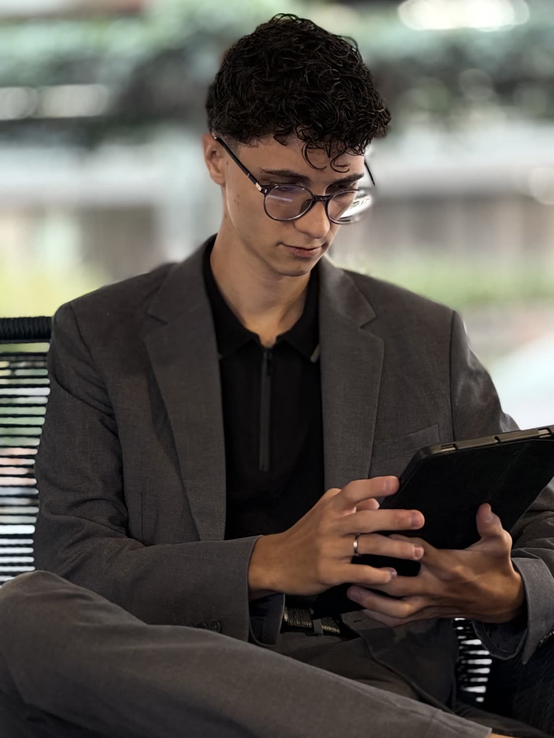 Arthur sentado, de óculos redondos e blazer cinza-escuro, usando um tablet