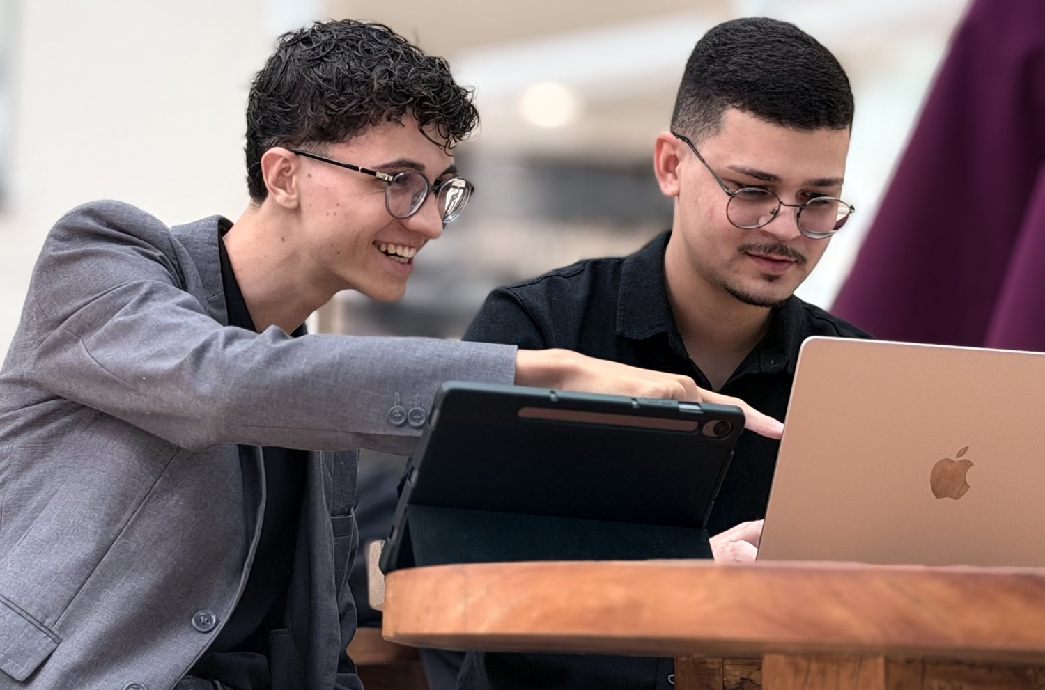 Arthur sorrindo e apontando para a tela enquanto Abdeel trabalha no notebook, os dois à mesa