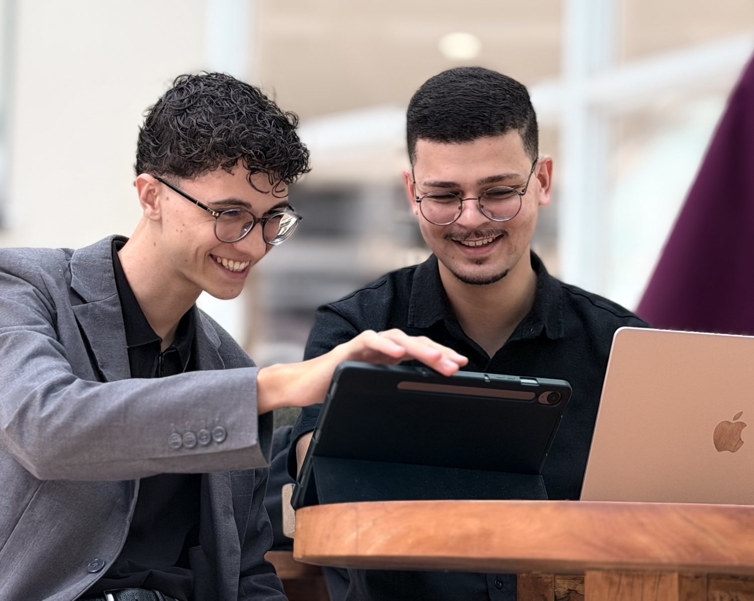 Arthur e Abdeel sorrindo à mesa, olhando juntos para um tablet, com um notebook ao lado